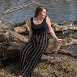 Woman sitting on a log in front of a river.