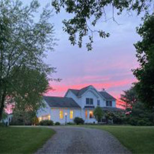 Photo of a farmhouse at the end of a dirt road at dusk